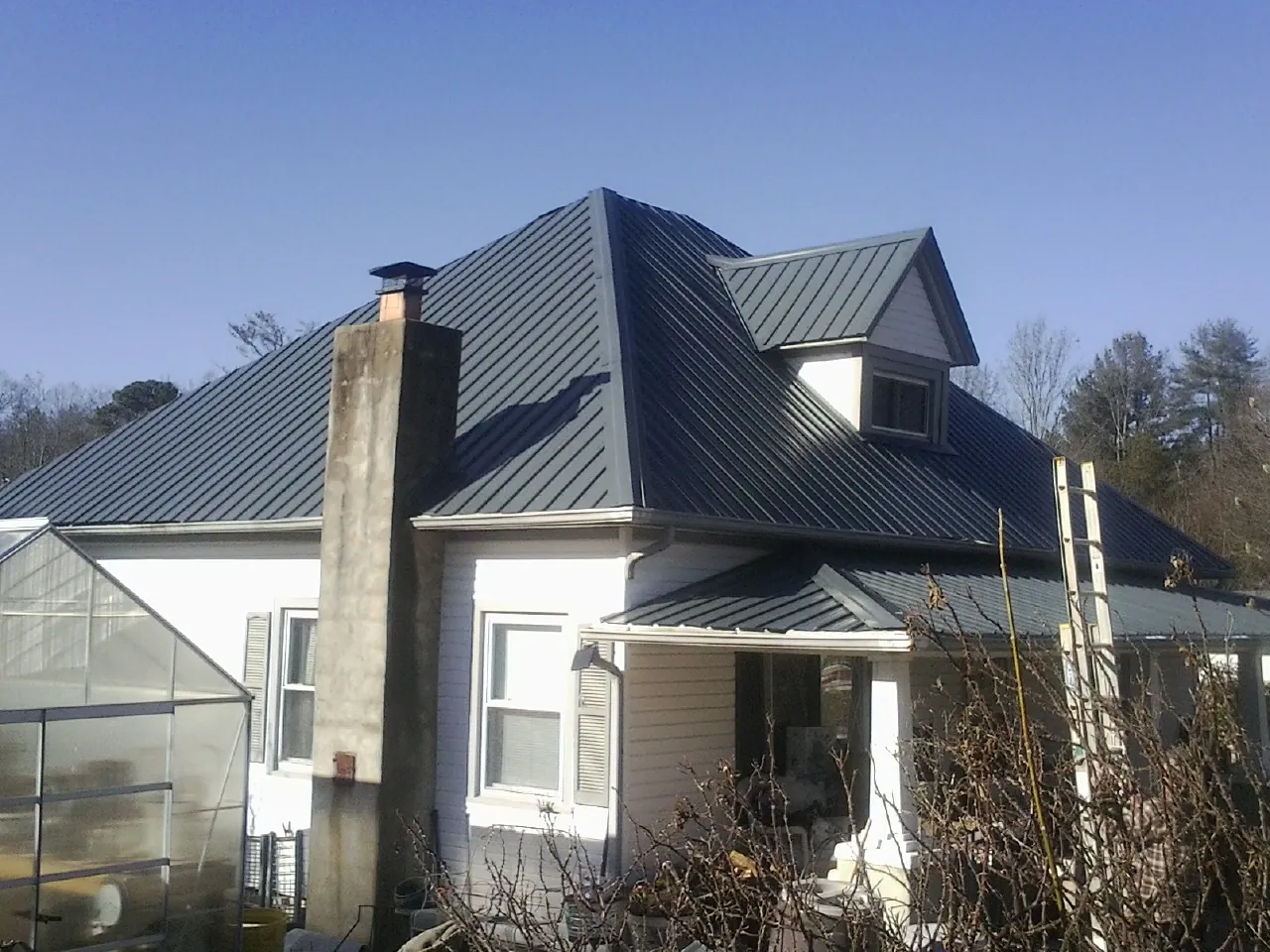Dark blue standing seam metal roof on a white farmhouse with dormer — Slate & Tile Roof Repair by Roofing Brothers in Absaraka