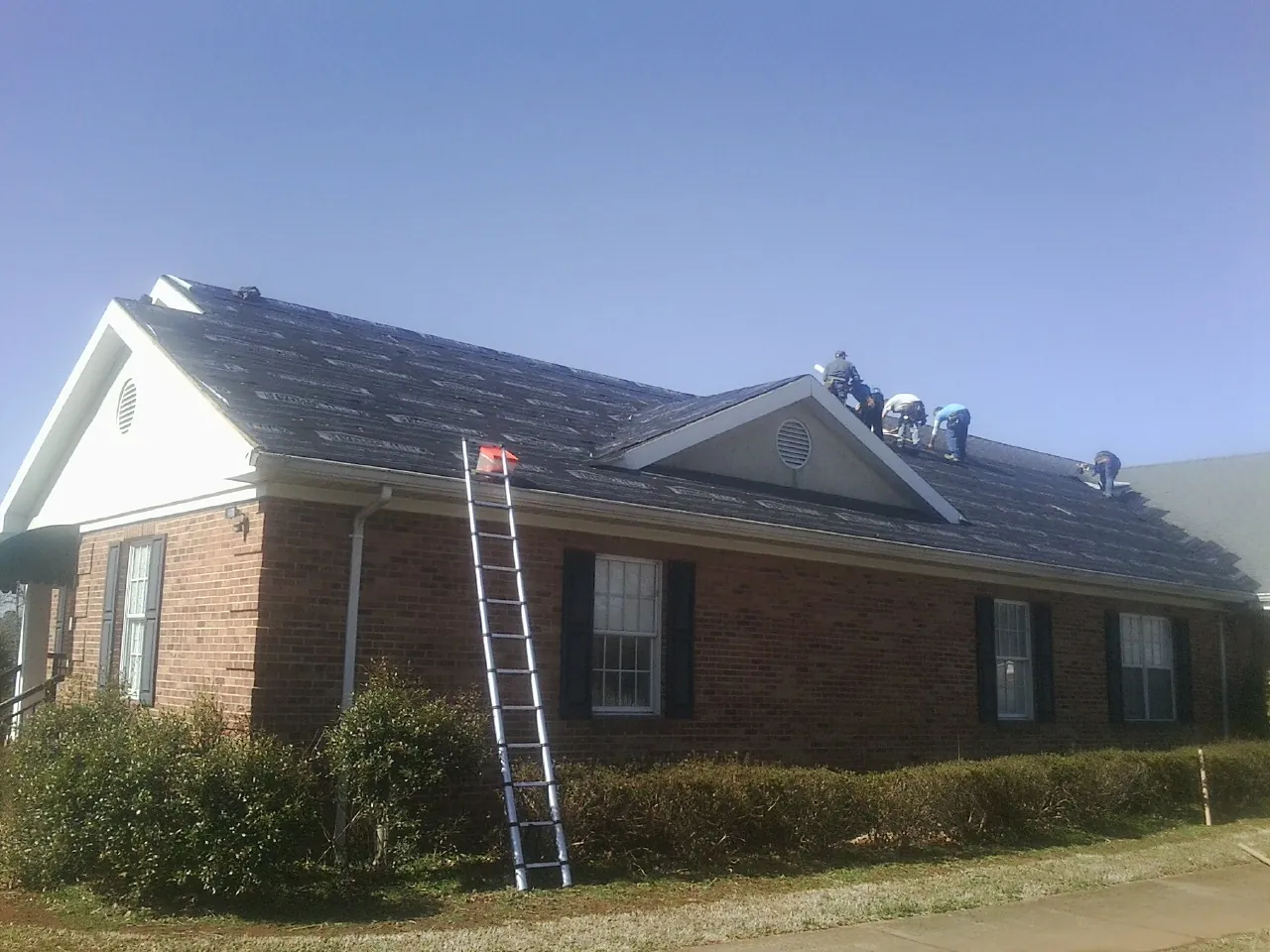 Crew tearing shingles off a brick ranch roof with a ladder set — Metal Roof Repair work by our crew in Absaraka
