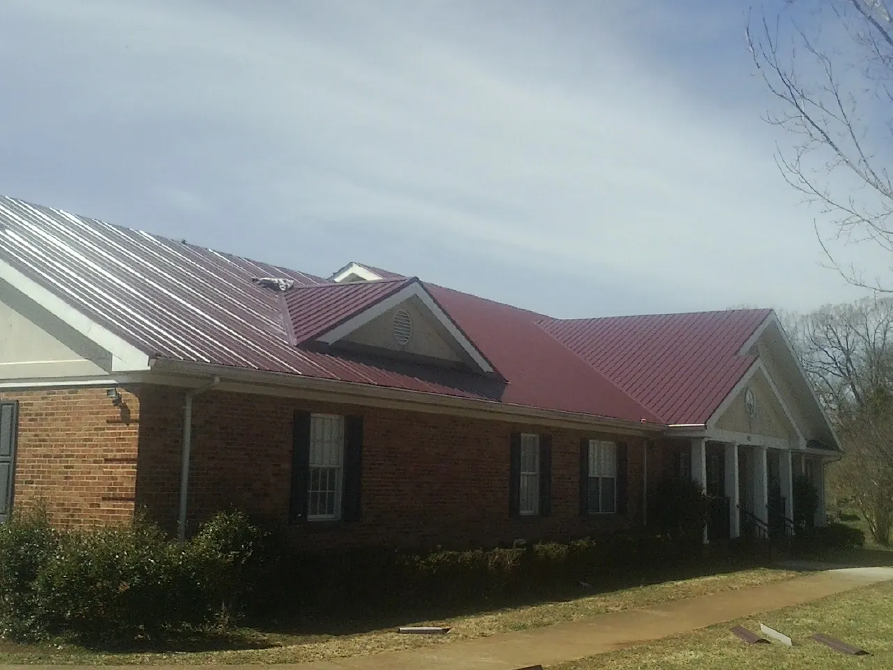 Red metal roof with gabled entries on a long brick building, from a Hail Damage Roof Repair job in Absaraka