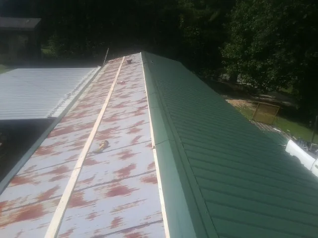 Old rusted panels beside newly installed green metal roofing — Wind Damage Roof Repair by Roofing Brothers in Absaraka