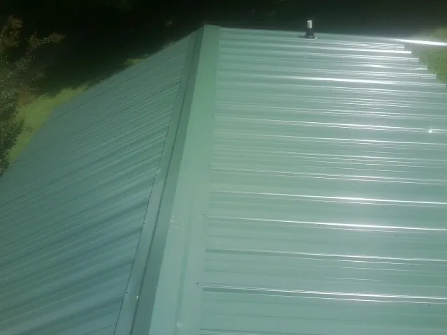 New green metal panels meeting at the ridge of a roof — Flat Roof Repair work by our crew in Absaraka