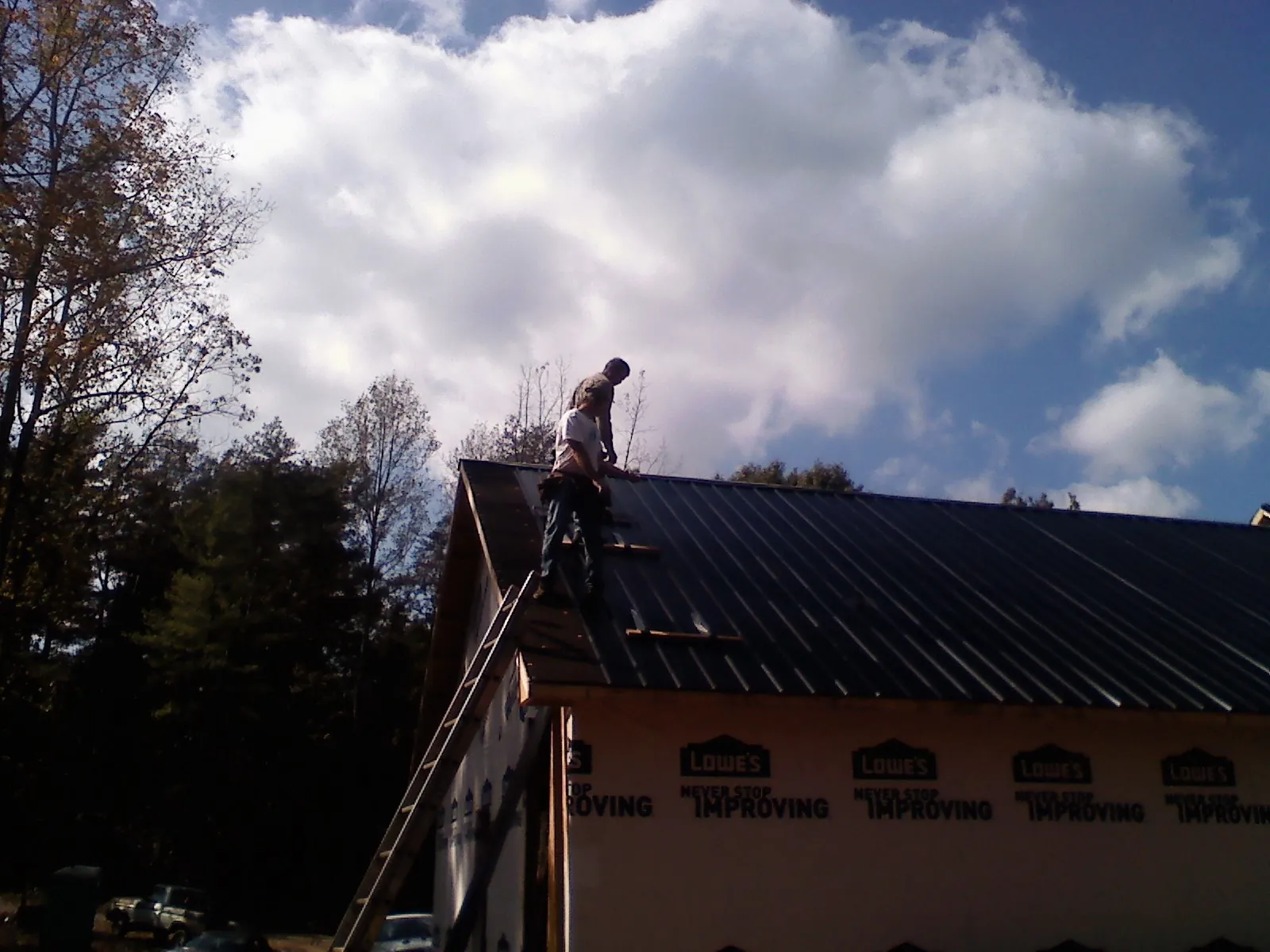 Roofer fastening dark metal panels high against a cloudy sky, from a Roof Inspection job in Absaraka