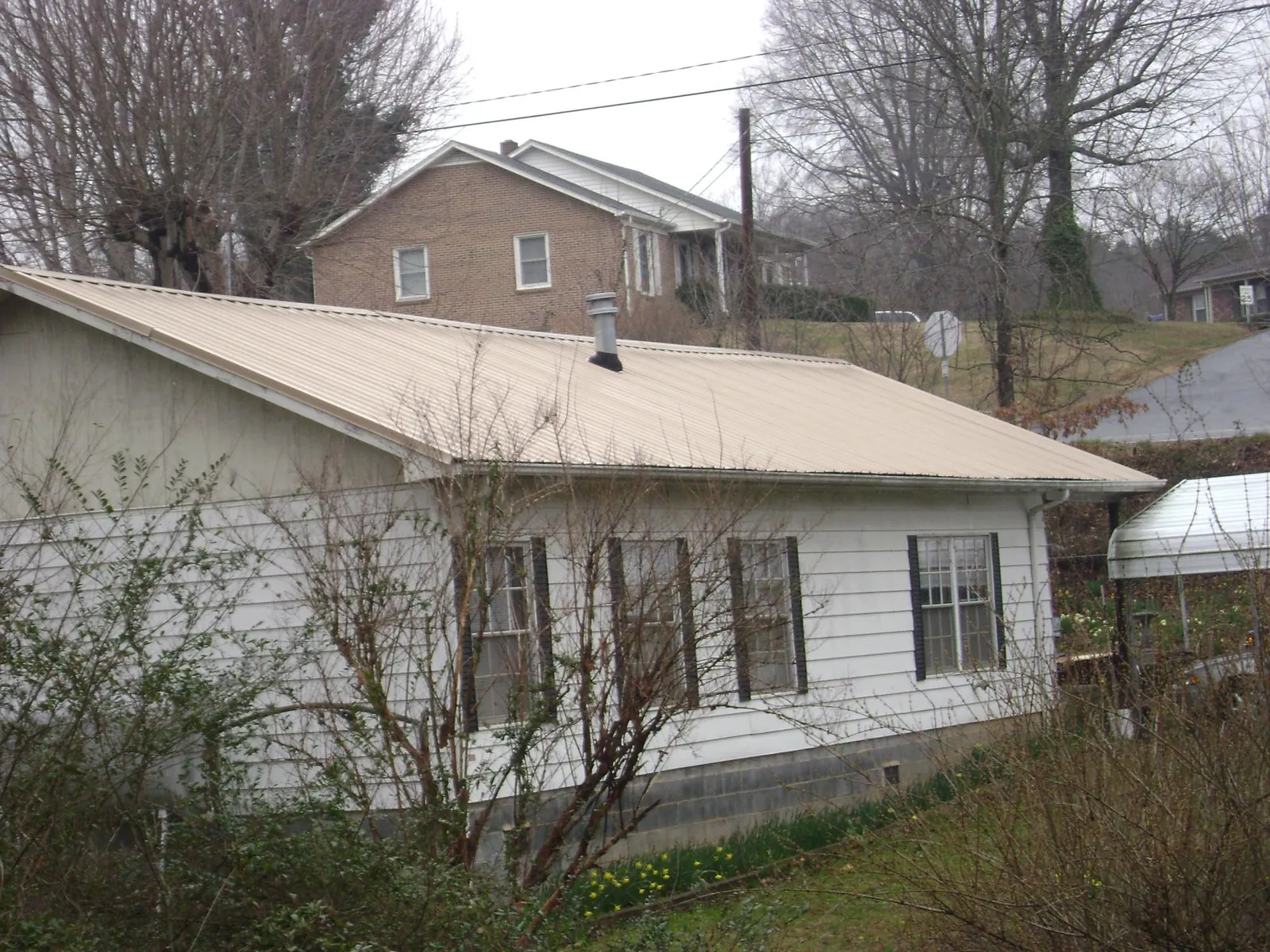 Tan metal roof on a white sided house set into a hillside — Commercial Roofing by Roofing Brothers in Absaraka